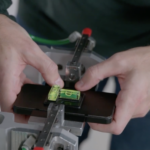 Corning worker holding a demonstration phone with Gorilla Glass on a testing rig, with spirit levels resting on top.